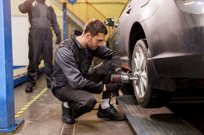 汽车服务,维修,维护人的汽车技工与电动螺丝刀更换轮胎车间汽车机械师与螺丝刀更换汽车轮胎